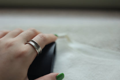 Minimalist Handmade Silver Ring — double-ridge band worn on a hand beside a case