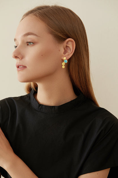 The Stones-Earrings — model wearing gold-tone drop earring with blue accent