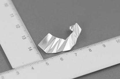 The Origami-Earrings — silver-tone folded earring photographed beside a ruler
