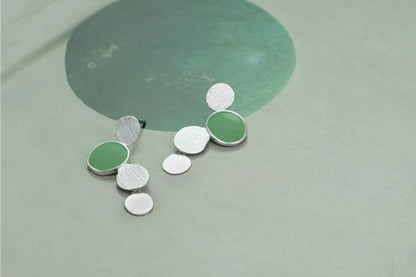 The Stones-Earrings — silver-tone earrings with green accents beside a stone