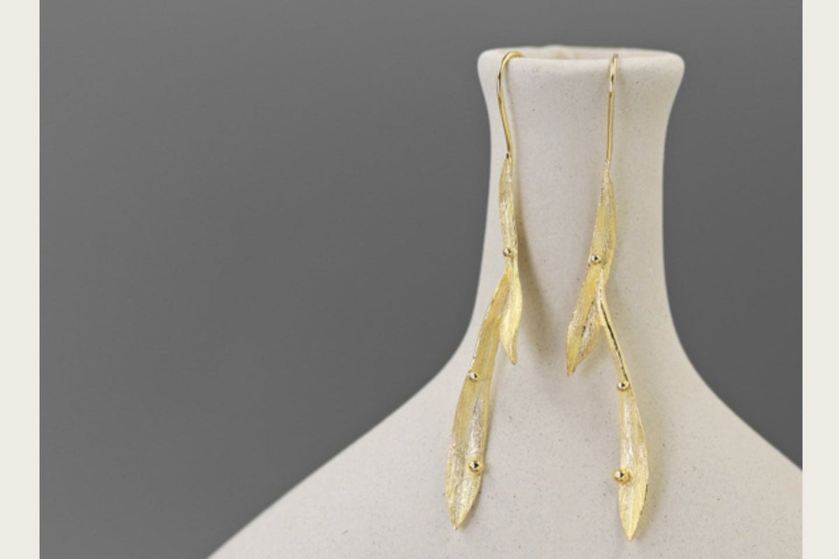 Wind Earrings — gold-tone elongated earrings on a display stand