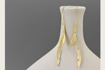 Wind Earrings — gold-tone elongated earrings on a display stand