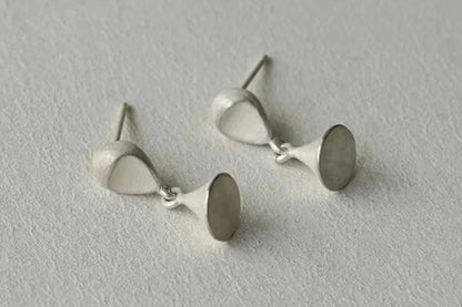 The Hourglass-Ear Stud — hourglass-shaped studs, front and back, on pale fabric