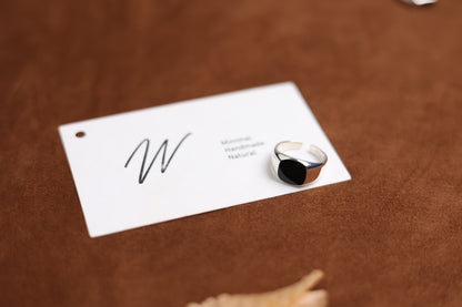 The Round Signet Onyx Ring — round black-stone signet ring beside card