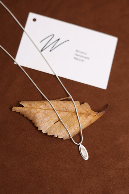 The B & W Onyx Necklace — white oval pendant necklace beside leaf and card