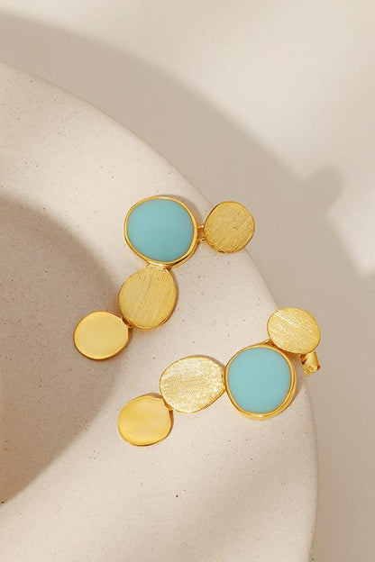 The Stones-Earrings — gold-tone earrings with blue accents on a display