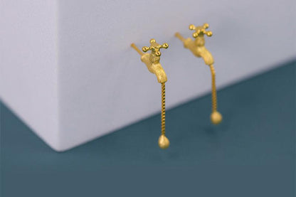 The Tab- Earrings — gold-tone tap-shaped earrings beside a block