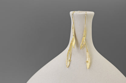 Wind Earrings — gold-tone elongated earrings on a display stand