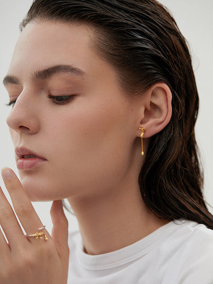The Tab- Earrings — gold-tone tap-shaped earring worn on an ear