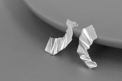 The Origami-Earrings — silver-tone folded earrings beside a plate