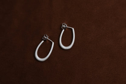 The Minimal U Ear Hoops — pair of U-shaped hoops on brown surface