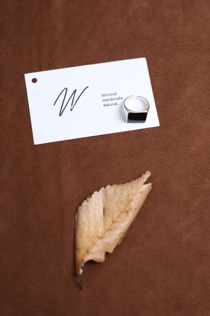 The Square Signet Ring with Black Onyx — square signet ring beside leaf and card