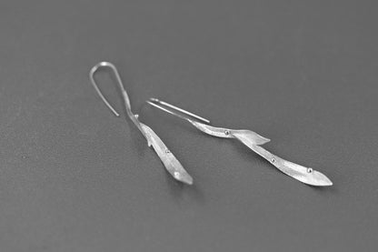 Wind Earrings — pair of silver-tone elongated earrings on grey surface