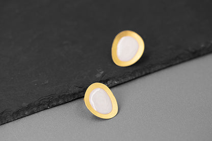The Color Drop-Earrings — pale oval earrings with gold-tone borders beside a stone