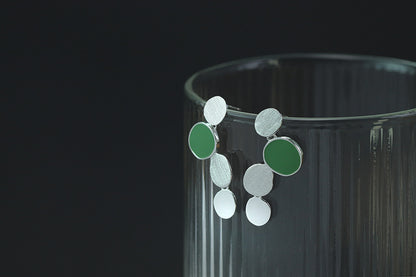 The Stones-Earrings — silver-tone earrings with green accents on a glass rim