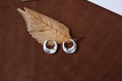The Minimalist Basic Hoop - The Drop — rounded hoop earrings beside a dried leaf