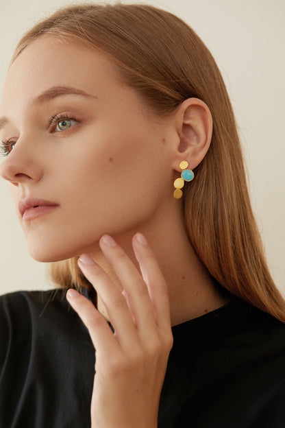 The Stones-Earrings — model wearing gold-tone drop earrings with blue accents