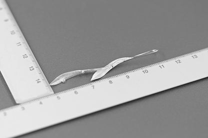 Wind Earrings — silver-tone elongated earrings photographed beside a ruler