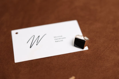 The Square Signet Ring with Black Onyx — square black-stone signet ring beside branded card