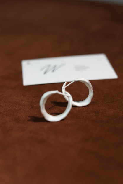 The Leaves-Earrings — pair of leaf-shaped hoops on brown surface
