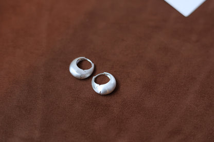 The Minimalist Basic Hoop - The Drop — silver-tone rounded hoops on a wooden surface