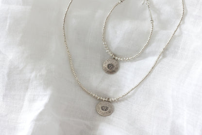 The Lotus Set — close-up of lotus-pendant necklace and bracelet on fabric