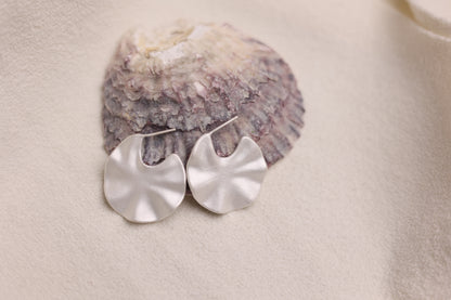 The Windmill-Earrings — pair of windmill-shaped earrings beside shell