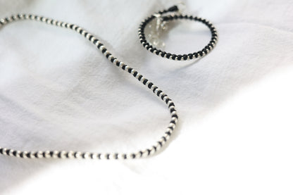 Handwoven Silver Set — black cord and silver-bead necklace and bracelet on fabric