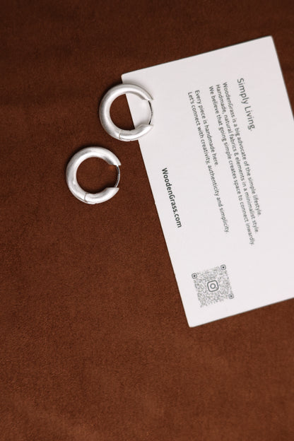 The Minimalist Basic Hoop — hoop earrings beside a brand card on wood