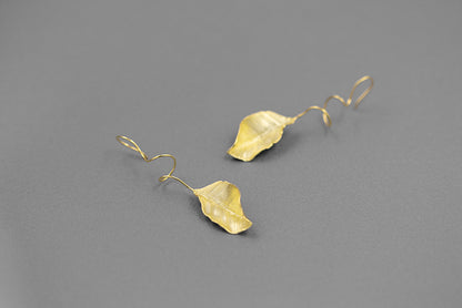 The Leaves -Earrings — gold-tone leaf earrings on grey surface