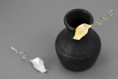 The Leaves -Earrings — gold-tone leaf earring on a vase with silver-tone earring beside it
