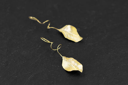 The Leaves -Earrings — gold-tone leaf earrings on a dark stone