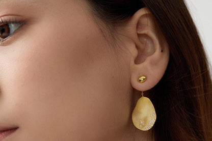 The Dune — gold-tone oval drop earring worn on an ear