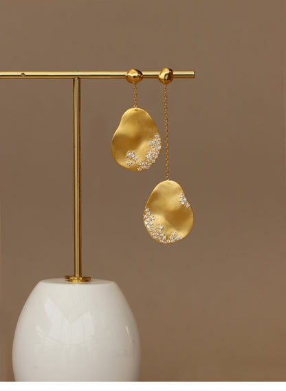 The Dune — gold-tone oval earrings hanging from a display